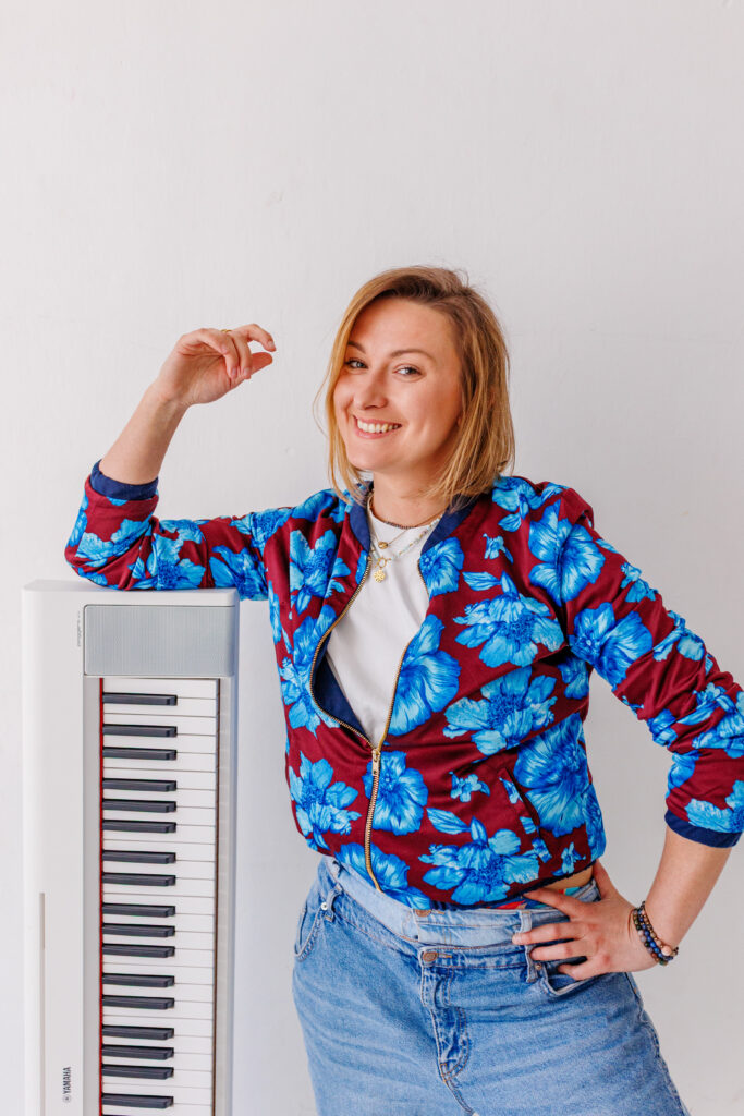 Uśmiechnięta kobieta opierająca ramię i łokieć na elektrycznym białm pianinie, pozstawionym na krótszym boku